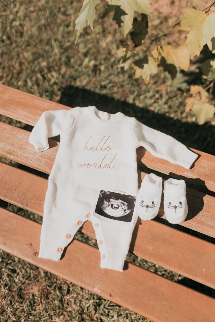 Flat lay of baby clothes and ultrasound photo on a bench outdoors.