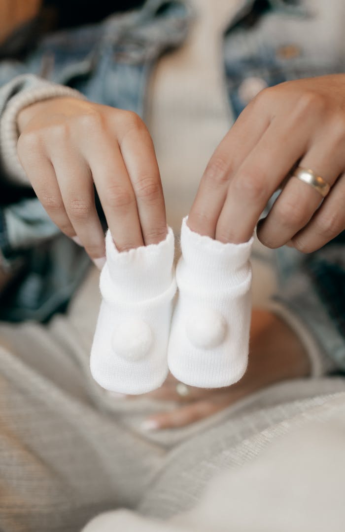 Close-up of hands holding small white baby socks, symbolizing a joyful anticipation of parenthood.